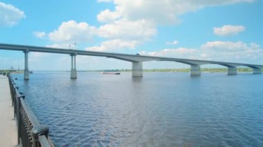 Köprü manzarası. Clip. Arabaların geçtiği nehirden geçen uzun bir köprü ve insanların yürüdüğü bir park var.