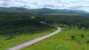 Arabalarla dolu uzun bir yol. İnsansız hava aracının görüntüsü. Sahne. Arka planda köhne dağlar ve ormanlar olan parlak bir yaz manzarası. Yazın açık gökyüzüne karşı arabalarla dolu bir yolun yanında..