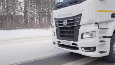 CZECH Cumhuriyet, PRAG - 21 Mart 2022: karlı bir yol boyunca beyaz bir kamyon sürüyor. Sahne. Büyük beyaz bir KAMAZ otoyol boyunca sürüyor. Ormanda arabaların gittiği bir yol var.