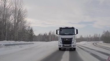 Rusya, MOSCOW - 21 Mart 2022: karlı bir yolda beyaz bir kamyon ilerliyor. Sahne. Büyük beyaz bir KAMAZ otoyol boyunca sürüyor. Ormanda arabaların gittiği bir yol var.