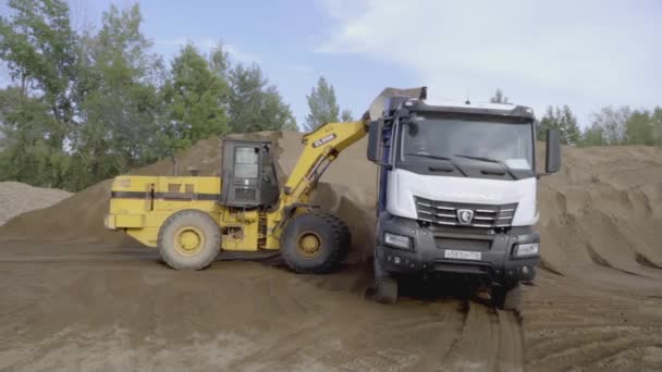 イギリス,ロンドン - MARCH 21, 2022: 掘削機はトラックに地球を追い込む. スクリーン。 黄色い掘削機の砂が青いカマズに注がれている. 採石場では,砂はトラックに集められます — ストック動画