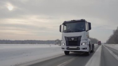 Rusya, MOSCOW - 21 Mart 2022: karlı bir yolda beyaz bir kamyon ilerliyor. Sahne. Büyük beyaz bir KAMAZ otoyol boyunca sürüyor. Ormanda arabaların gittiği bir yol var.
