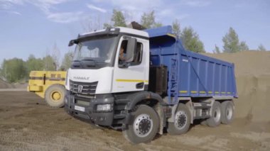 İngiltere, Londra - 21 Mart 2022: Kazı işçisi toprağı kamyona boşalttı. Sahne. Sarı bir kazıcıdan çıkan kum mavi bir KAMAZ 'a dökülüyor. Taş ocağında, kum kamyonlarda toplanır.