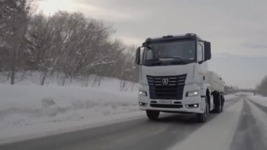 Rusya, MOSCOW - 21 Mart 2022: karlı bir yolda beyaz bir kamyon ilerliyor. Sahne. Büyük beyaz bir KAMAZ otoyol boyunca sürüyor. Ormanda arabaların gittiği bir yol var.