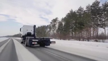 Rusya, MOSCOW - 21 Mart 2022: karlı bir yolda beyaz bir kamyon ilerliyor. Sahne. Büyük beyaz bir KAMAZ otoyol boyunca sürüyor. Ormanda arabaların gittiği bir yol var.