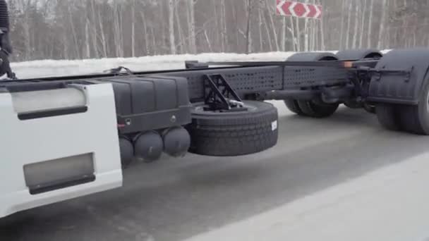 A huge white truck is driving along the road. SCENE. Black wheels Kamaz close-up. White truck rides on the road in winter. A lot of truck wheels are shown in the frame — Stock Video