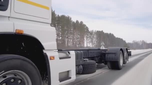 Oroszország, MÁRCIUS - MÁRCIUS 21, 2022: Egy hatalmas fehér teherautó halad végig az úton. Helyszín. Fekete kerekek Kamaz közelkép. Fehér teherautó lovagol az úton télen. Sok teherautó kerekek jelennek meg a keret — Stock videók