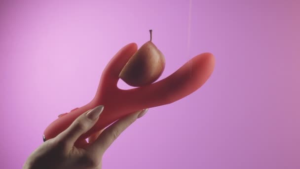 Рожевий фон. Креативний. Вібратор, тримається за руку, в який вони кладуть яскраво-червоне яблуко і наливають слизьким білим кремом. — стокове відео