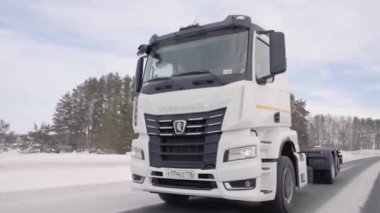 Rusya, MOSCOW - 21 Mart 2022: karlı bir yolda beyaz bir kamyon ilerliyor. Sahne. Büyük beyaz bir KAMAZ otoyol boyunca sürüyor. Ormanda arabaların gittiği bir yol var.