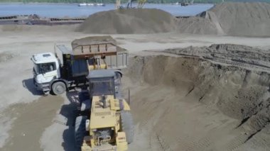 Kazıcı, toprağı kamyona boşaltıyor. Sahne. Sarı bir kazıcıdan çıkan kum mavi bir KAMAZ 'a dökülüyor. Taş ocağında, kum kamyonlarda toplanır.