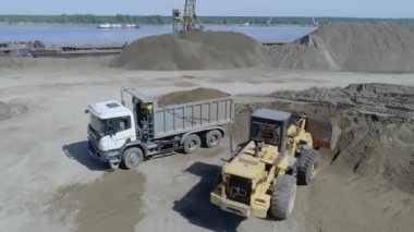 Bir kazıcı bir taş ocağından kum kaldırır. Sahne. Kazıcının yanında bir KAMAZ var. Kum bir taş ocağında mayınlanır. Arka planda taş ocağında bir göl var.