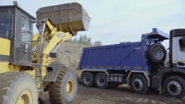 RUSSIA, MOSCOW - 21 Mart 2022: kazıcı dünyayı kamyona döküyor. Sahne. Sarı bir kazıcıdan çıkan kum mavi bir KAMAZ 'a dökülüyor. Taş ocağında, kum kamyonlarda toplanır.