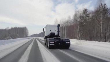 CZECH Cumhuriyet, PRAG - 21 Mart 2022: karlı bir yol boyunca beyaz bir kamyon sürüyor. Sahne. Büyük beyaz bir KAMAZ otoyol boyunca sürüyor. Ormanda arabaların gittiği bir yol var.