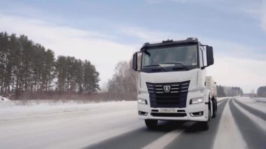 Rusya, MOSCOW - 21 Mart 2022: karlı bir yolda beyaz bir kamyon ilerliyor. Sahne. Büyük beyaz bir KAMAZ otoyol boyunca sürüyor. Ormanda arabaların gittiği bir yol var.