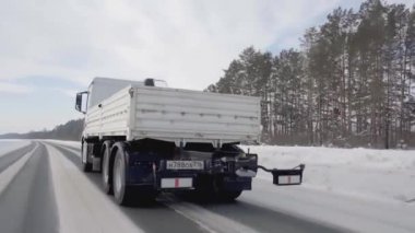 Rusya, MOSCOW - 21 Mart 2022: karlı bir yolda beyaz bir kamyon ilerliyor. Sahne. Büyük beyaz bir KAMAZ otoyol boyunca sürüyor. Ormanda arabaların gittiği bir yol var.