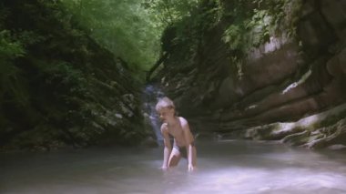 Bir çocuk şelalenin yanındaki gölete su sıçratıyor. - Yaratıcı. Küçük beyaz bir çocuk gölde oturuyor. Beyaz saçlı çocuk gölde oynuyor.