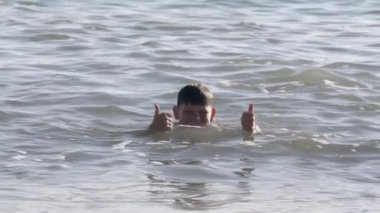 Siyah saçlı bir çocuk anne ve babasıyla birlikte denizde yüzüyor. - Yaratıcı. Çocuk mutlu ve kıyıda duran ailesine her şeyin yolunda olduğunu gösteriyor.