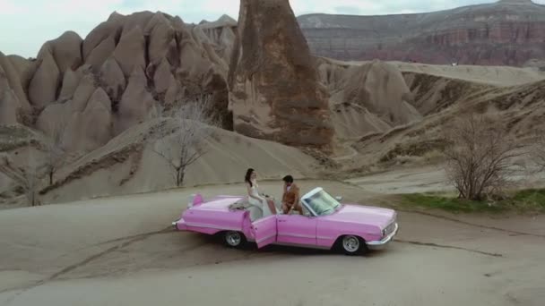 Foto aerea di una coppia su un'auto d'epoca rosa. Azione. Riprese di nozze di un uomo e una donna in un paese caldo nel deserto. Coppia felice su una passeggiata — Video Stock