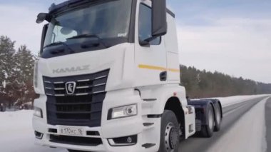 Rusya, MOSCOW - 21 Mart 2022: karlı bir yolda beyaz bir kamyon ilerliyor. Sahne. Büyük beyaz bir KAMAZ otoyol boyunca sürüyor. Ormanda arabaların gittiği bir yol var.