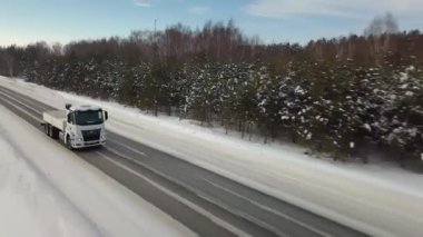 Rusya, MOSCOW - 21 Mart 2022: karlı bir yolda beyaz bir kamyon ilerliyor. Sahne. Büyük beyaz bir KAMAZ otoyol boyunca sürüyor. Ormanda arabaların gittiği bir yol var.