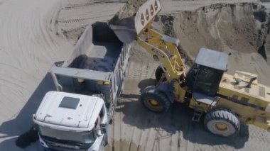 İngiltere, Londra - 21 Mart 2022: Kazı işçisi toprağı kamyona boşalttı. Sahne. Sarı bir kazıcıdan çıkan kum mavi bir KAMAZ 'a dökülüyor. Taş ocağında, kum kamyonlarda toplanır.