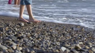 Childs 'ın ayakları dalgalarla buluşmak için kayalık kıyı boyunca yürüyor. - Yaratıcı. Bir çocuk akşam sahilinde deniz dalgalarının arka planında yürür.