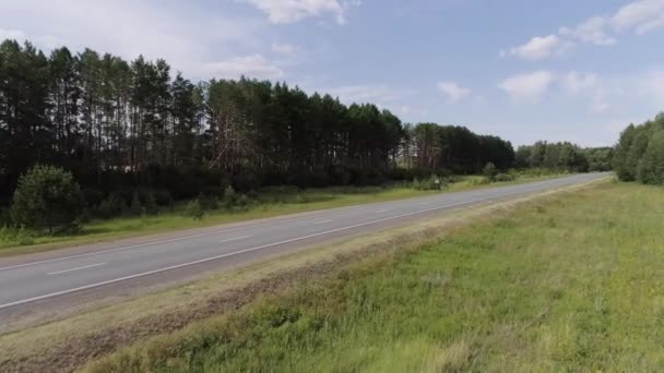 En lång asfalterad väg. En lång väg intill en grön ljusskog runt omkring och bakom dig kan du se en klarblå himmel. — Stockvideo