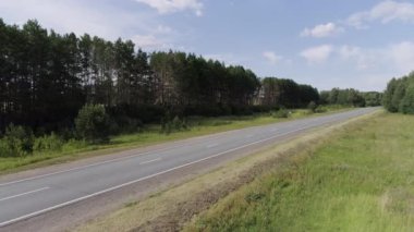 Uzun asfalt bir yol. Sahne. Yeşil bir ormanın yanında uzun bir yol. Etrafında ve arkasında parlak mavi bir gökyüzü görebilirsiniz..