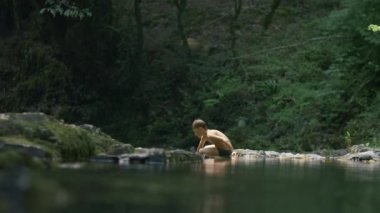Çocuk soğuk doğal gölette yüzer. Yaratıcı. Çocuk ormandaki doğal gölete dalıyor. Çocuk yeşil ormanda gölde yüzüyor.