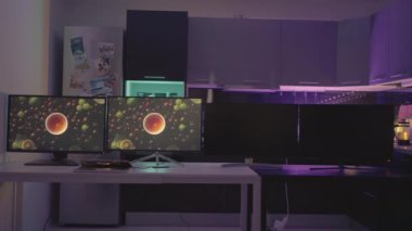 ALMANY, BERLİN - 21 Mart 2022: 4 monitör gri bir mutfakta. Aksiyon. İki kişi çalışıyor ve iki koyu renk monitör masada. Karanlık mutfakta bir masa, buzdolabı, monitörler ve dolaplar var.