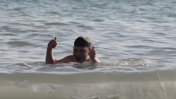 Темноволосый мальчик плавает в море и плывет к берегу. СОЗДАНИЕ. Мальчик показывает родителям, которые стоят на берегу, что с ним все в порядке. — стоковое видео