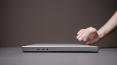 El bilgisayarı açar. Aksiyon. Bir adam bir eli gri arka planda olan bir dizüstü bilgisayar açar. Gümüş bir dizüstü bilgisayar karanlık bir masada oturuyor. Netbook 'un üst kapağını kaldırdım.
