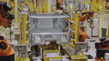 Moskova - Rusya, 01.14.2022: Fabrikadaki robotlar arabayı monte ediyor. Sahne. Fabrikada, turuncu robotik kollarla beyaz bir araba monte edilir. Arabalar ve kamyonlar fabrikada toplandı.