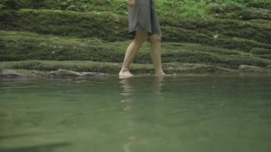 İnsan ormanda kayalık bir arazide suyun üzerinde yürür. Yaratıcı. Kadınlar yaz ormanlarında doğal gölette su üzerinde yürürler. Vahşi yeşil ormanda yürüyüşe çıkmış bir kadın.