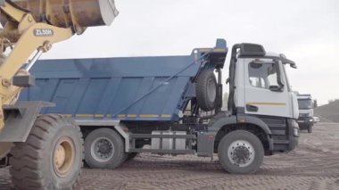 Rusya, Moskova - 7 Mayıs 2022 Kazıcı inşaat alanında toprakla dolu çöp kamyonunu yükledi. Sahne. Kamyonlar çalışıyor ve inşaat alanını temizliyorlar. Kazıcı toprağı çöp kamyonuna boşaltıyor.