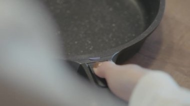 Mutfak için yeni kızartma tavasını, çıkarılabilir sapı olan bir kadının elini kapatıyoruz. Başla. Ev aletleri kavramı.