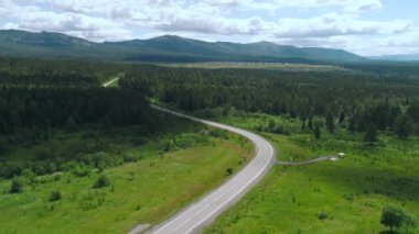 Bulutlu arka planda uzun bir bükme yolu ve yeşil çayır ya da tarlanın havadan görünüşü. Sahne. Güzel yaz doğası.