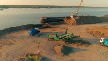 İnşaat alanında çalışan kazıcı, kamyon ve vinçler. Sahne. Kum ocağı ve arka plandaki nehir..