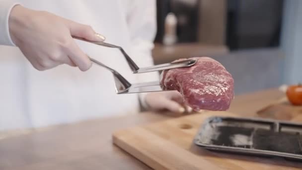 Närbild av kvinna kvinnlig kock sätta ribeye på stekpanna med non stick beläggning. Börja. Tillagning av rå köttbiff hemma i köket. — Stockvideo