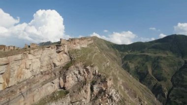 Arka planda bulutlar olan büyük, güzel bir kayanın havadan görünüşü. Başla. Yeşil yamaçlarla dağların üzerinde uçuyor.
