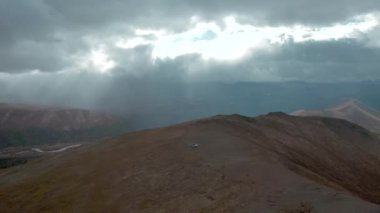 Helikopterin dağın tepesindeki görüntüsü. Şarjör. Helikopter bulutlu ufuk görüşüyle dağda durdu. Dağları olan güzel bir manzara ve bulutlu bulutlarda güneş ışığı