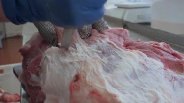 Kasap et leşi keserken yakın plan. Şarjör. Eller bıçakla kesilmiş et. Eldivenli kasap büyük bir parça eti bıçakla keser.