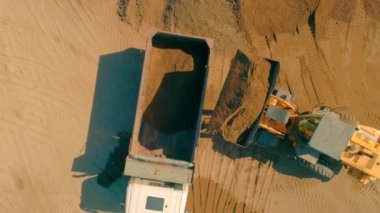 Kazıcı kumu çöp kamyonuna boşaltıyor. Sahne. Kamyona kum yükleyen kazıcının üst görüntüsü. İnşaat ve öğütme kum ile çalışır.