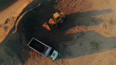 Kazıcı kumu çöp kamyonuna boşaltıyor. Sahne. Kamyona kum yükleyen kazıcının üst görüntüsü. İnşaat ve öğütme kum ile çalışır.