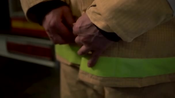 Detailní záběr hasiče, jak si obléká uniformu ochranného obleku pro ochranu před požárem. Klip. Muž hasič zapíná knoflíky svého obleku. — Stock video