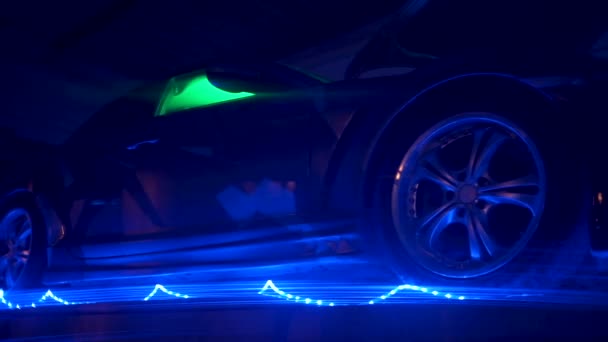 Vue du bas d'une voiture moderne avec éclairage au néon dans un garage sombre. Clip. Concept de tuning et de transport de voiture. — Video