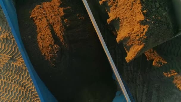 Екскаватор видаляє пісок у сміттєвоз. Сцена. Вид зверху екскаватора завантажує пісок у вантажівку. Будівельні та шліфувальні роботи з піском — стокове відео