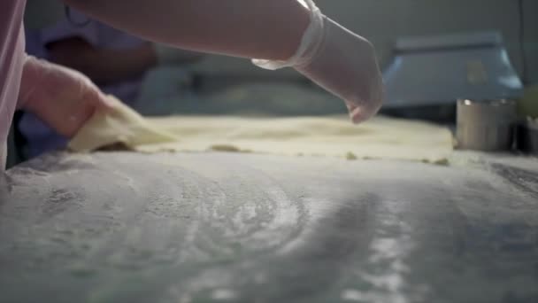 Feche de uma mão na luva pondo a farinha em uma mesa e uma folha do teste. Clipe. Processo de produção de bolinhos na fábrica. — Vídeo de Stock