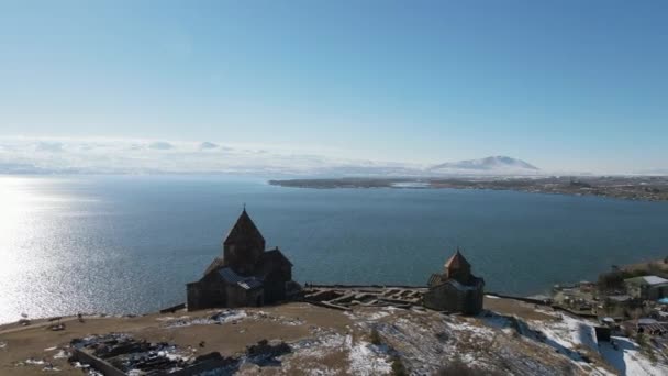 Vista aérea de una colina alta y un templo de madera en su parte superior. Filmación. Hermoso mar con superficie ondulada y cielo azul nublado. — Vídeos de Stock