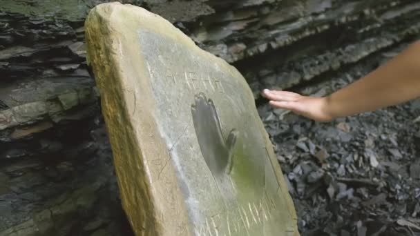 Eine Person lehnt ihre Hand an einen Stein mit einer Aussparung in Form einer Hand. CREATIVE. Sie legten ihre Hände auf die Steinplatte. Die Hand wurde in eine Aussparung auf dem Stein gelegt — Stockvideo
